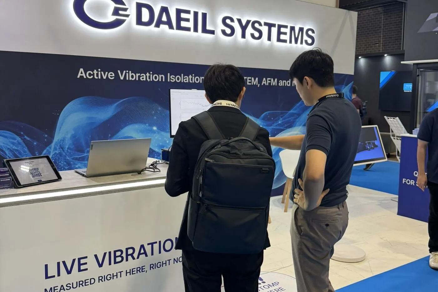 A DAEIL SYSTEMS team member explains the live vibration signals on screen to a visitor at the LIVE VIBRATION DATA counter