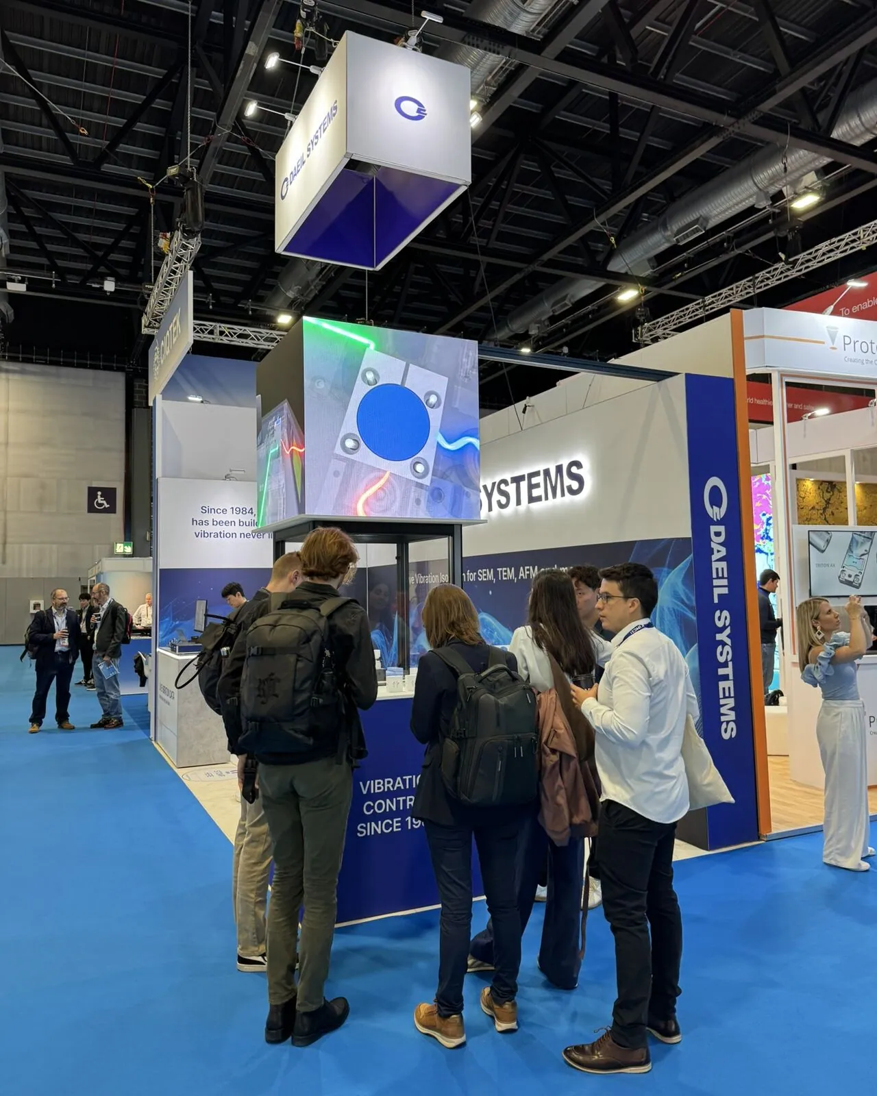 Visitors in conversation at the DAEIL SYSTEMS stand, beneath the glowing LED video cube